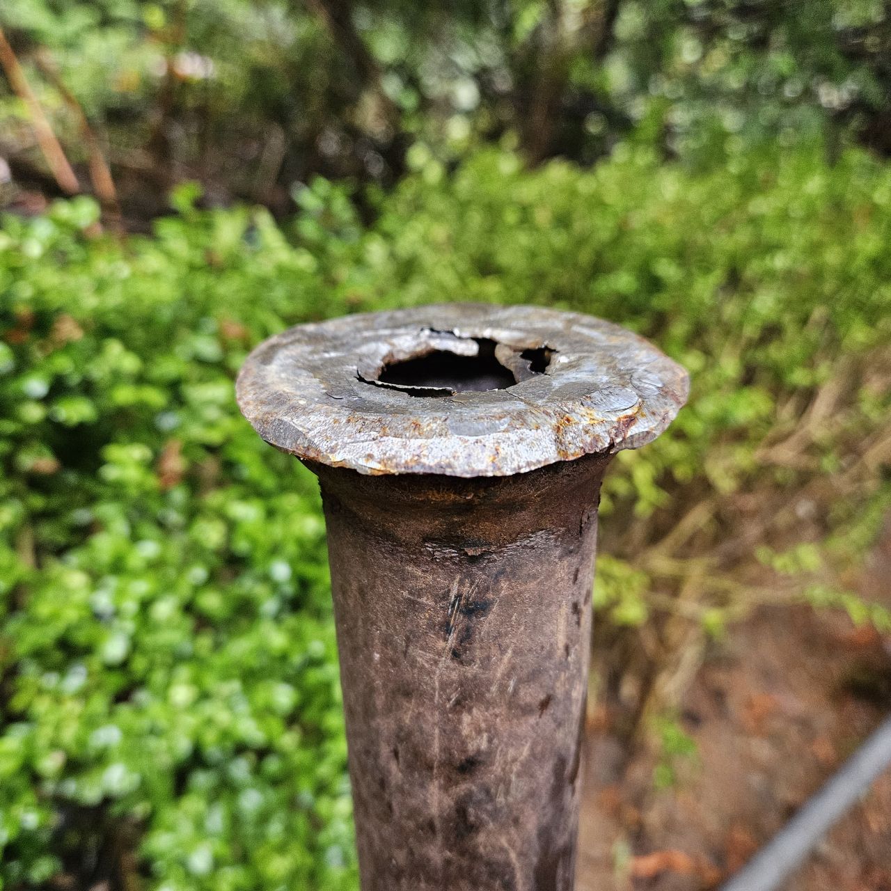 The end of a metal pipe, pounded into the ground. It is significantly flattened, yet evenly distributed producing a very rough flange. The end of a metal pipe, pounded into the ground. It is significantly flattened, yet evenly distributed producing a very rough flange.